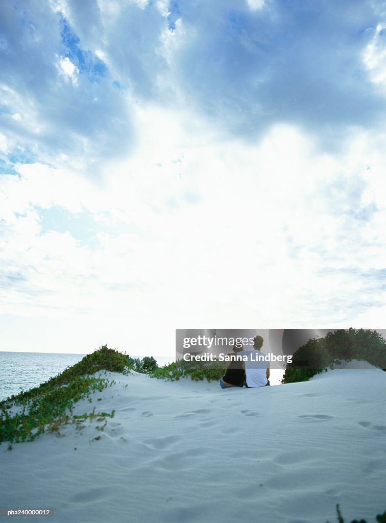 Couple on sand dune looking out to sea, rear view