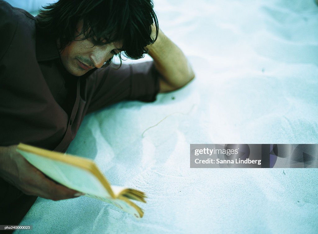 Man lying on sand, reading, close-up