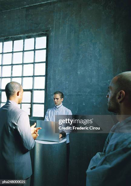 three men in room, one using laptop computer - being watched stockfoto's en -beelden