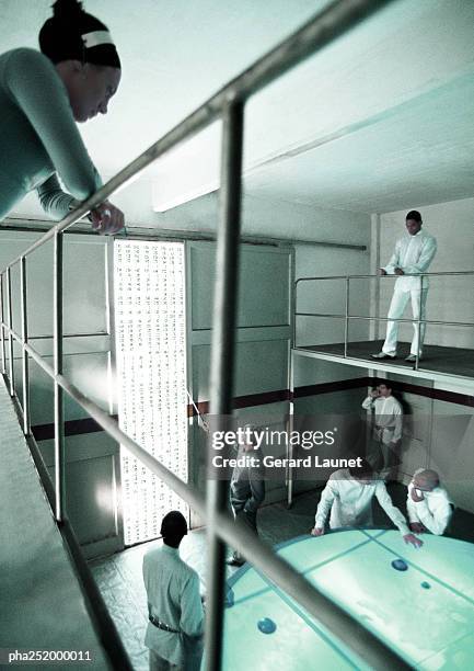 woman leaning on railing, people standing around table - being watched stockfoto's en -beelden