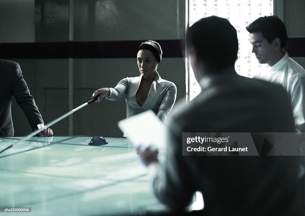 Four people around table, woman holding stick