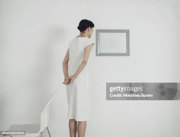 woman standing looking at frame on wall, rear view - mani dietro la schiena foto e immagini stock