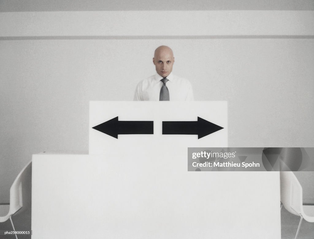 Man standing behind podium with two arrow signs pointing in opposite directions