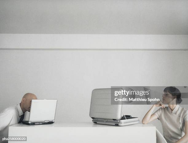 woman and man sitting at desk, woman looking at open briefcase, man looking at laptop - double facepalm stock pictures, royalty-free photos & images