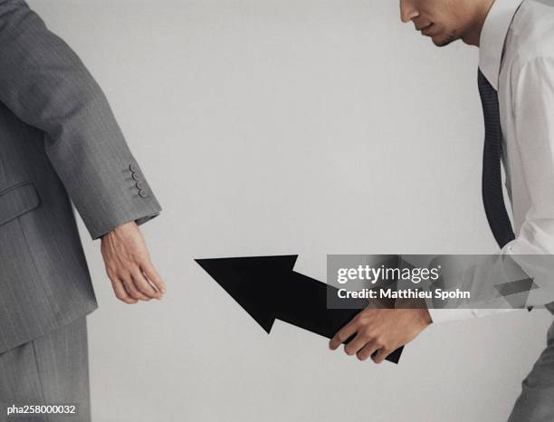 businessman passing arrow sign to another businessman, midsection - aother stock pictures, royalty-free photos & images
