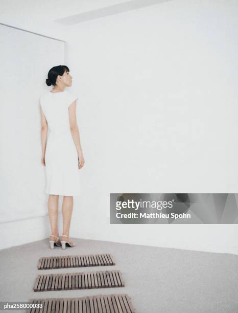 woman standing in corner of room at end of path of wooden rectangles - femme robe blanche photos et images de collection
