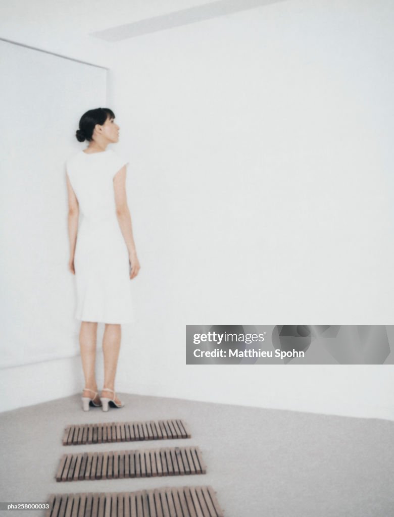 Woman standing in corner of room at end of path of wooden rectangles
