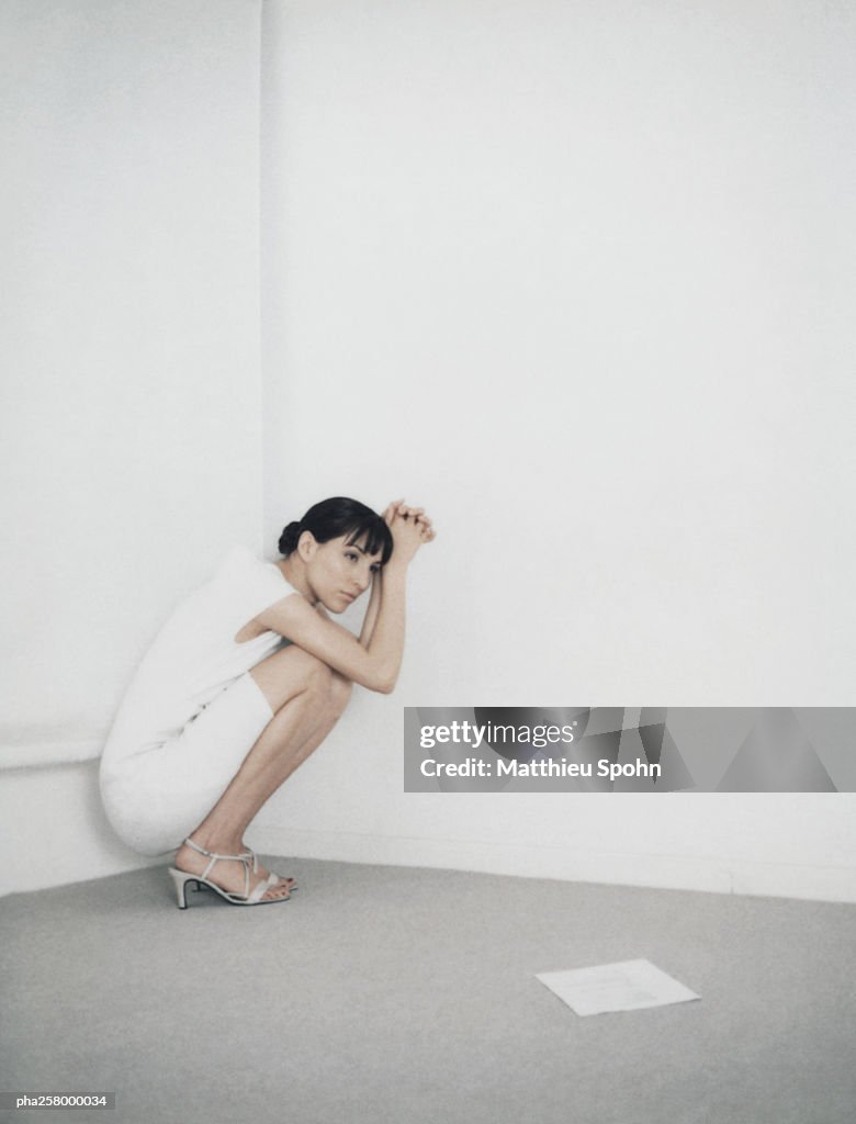 Woman crouching in corner of room, piece of paper on floor