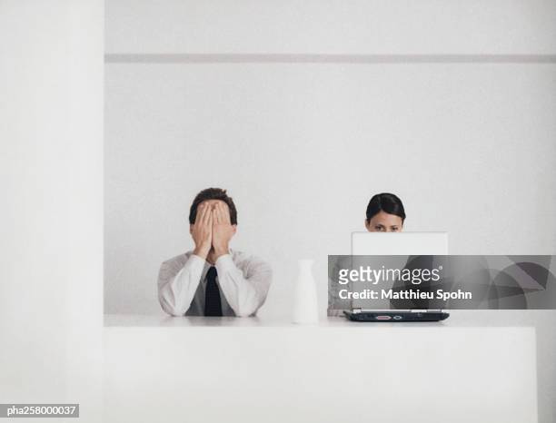 man and woman sitting at counter, man covering face, woman behind laptop - ignorieren stock-fotos und bilder