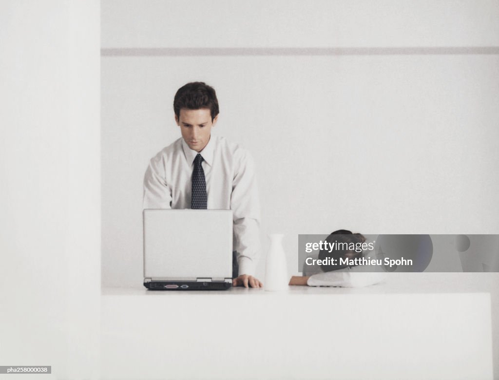 Man standing behind counter behind laptop, woman with head down on arm