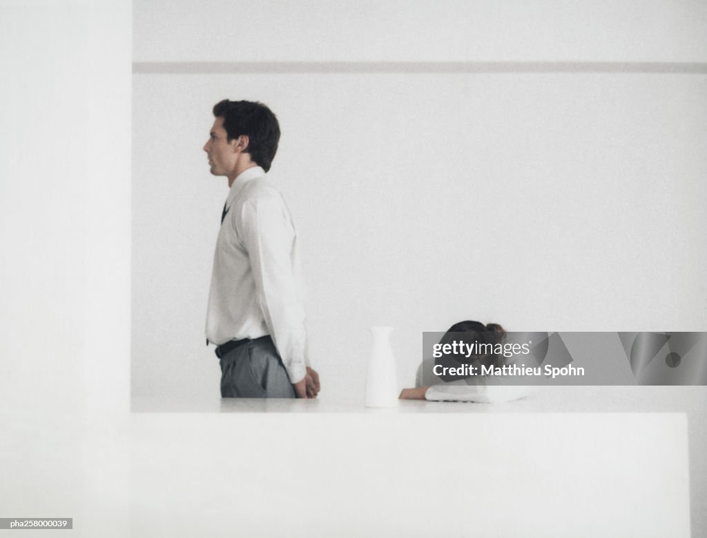 Man standing behind table, side view, woman with head down on arm