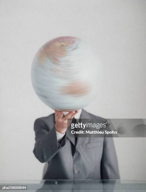 man in suit at table holding globe with one hand in front of head - world at your fingertips stockfoto's en -beelden