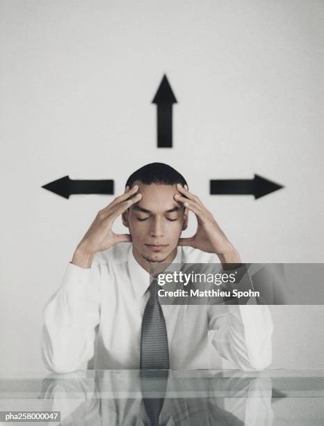 man sitting at table holding head with eyes closed, arrow signs around head - double facepalm stock pictures, royalty-free photos & images