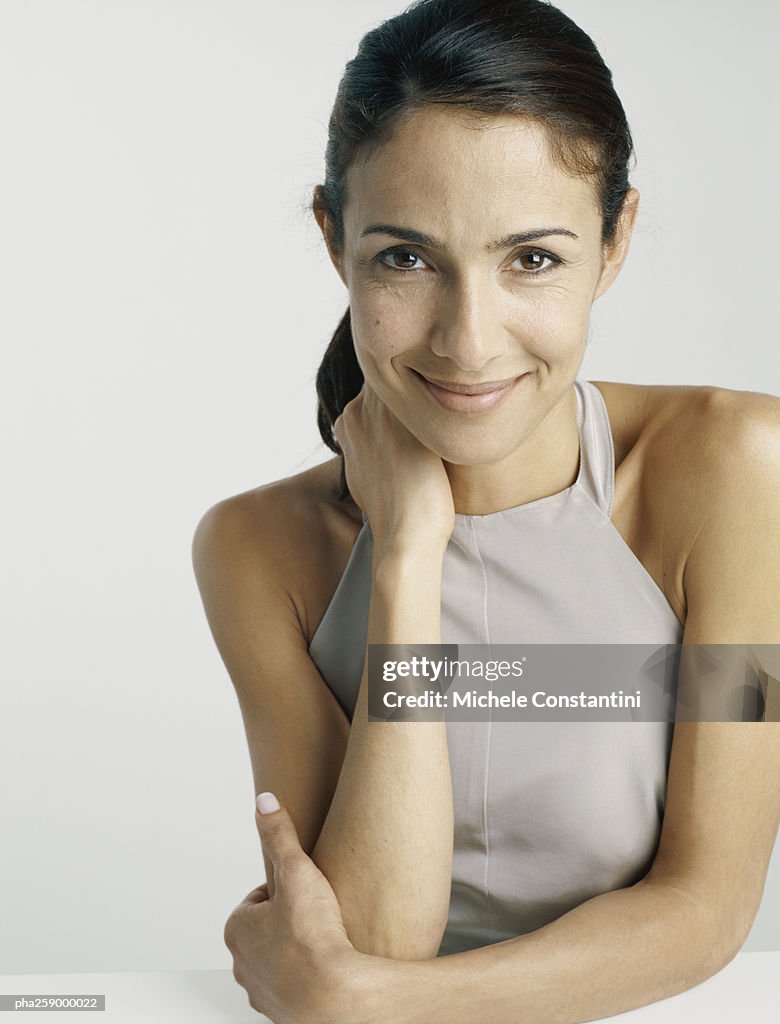 Young woman smiling at camera with one arm in front of chest and one hand holding neck