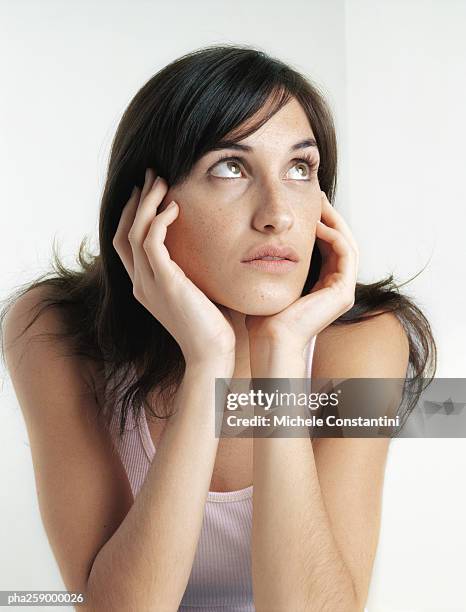 young woman looking up and away, holding face between hands - hand on chin stock pictures, royalty-free photos & images