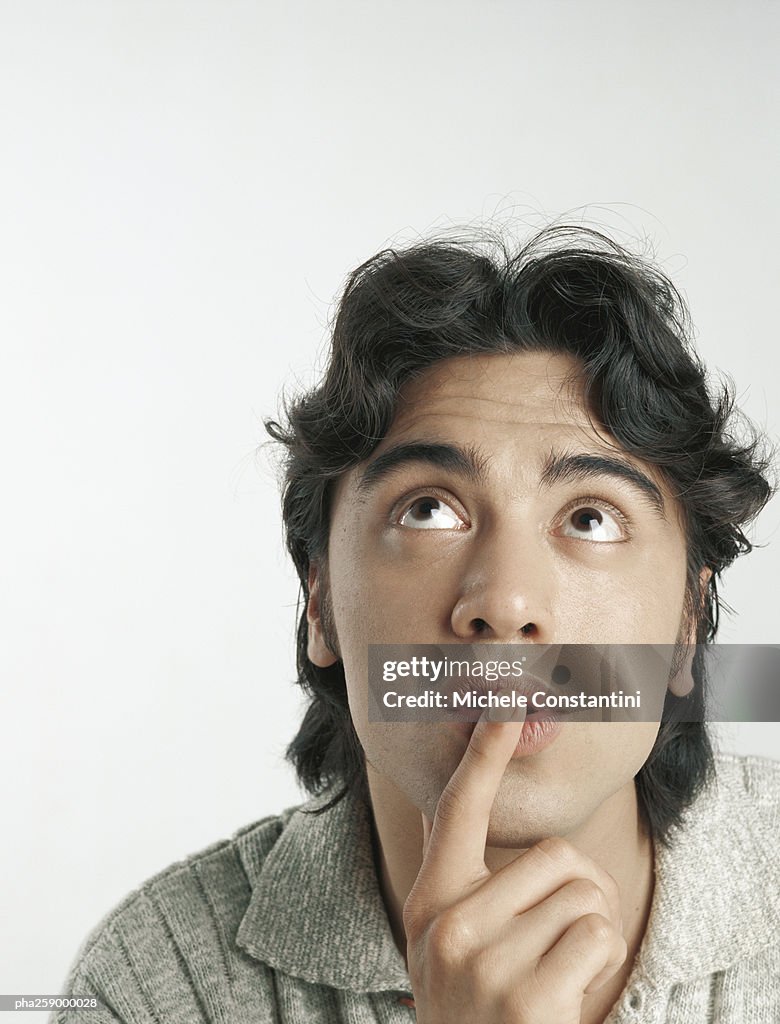 Young man looking up with finger on lips