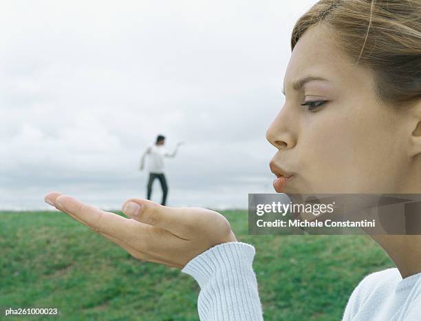 woman in foreground holding out palm and blowing kiss, man in distant background, optical illusion - distant imagens e fotografias de stock