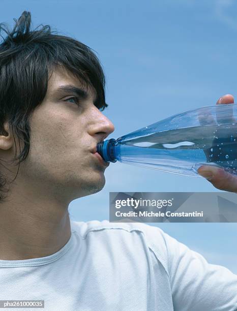 young man drinking from bottle, looking out of frame, close-up - out of frame stock-fotos und bilder