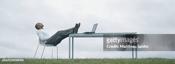 man sitting in chair outdoors with feet on table and laptop on table, in front of overcast sky - legs on the table stock pictures, royalty-free photos & images
