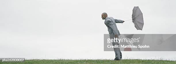man standing on grass holding inside-out umbrella behind him - inside out stock pictures, royalty-free photos & images