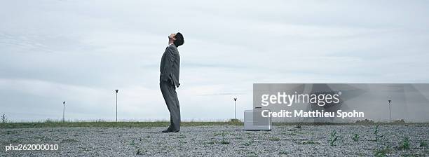 man standing in abandoned lot looking up at sky, metallic briefcase on ground behind him - the lot stock-fotos und bilder