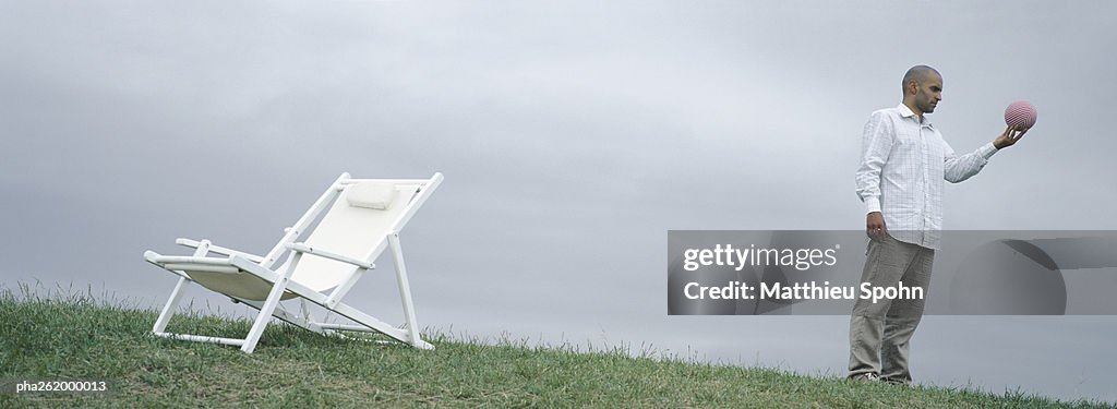 Man standing on grass near lounge chair holding ball in hand