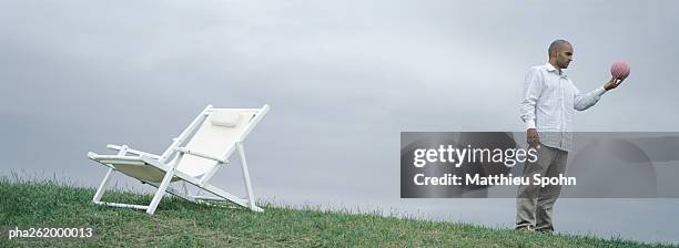 man standing on grass near lounge chair holding ball in hand - ball chair stock pictures, royalty-free photos & images