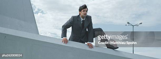 man in suit climbing over low concrete wall - huir fotografías e imágenes de stock