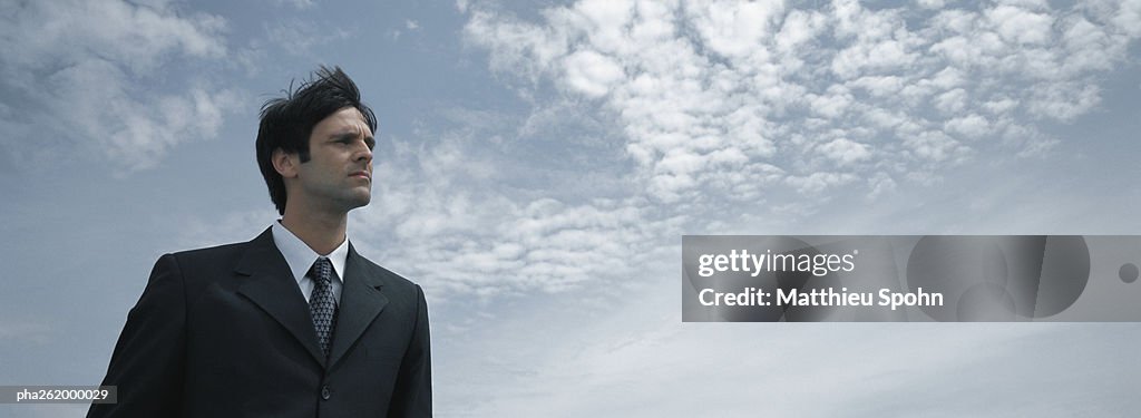 Man in suit standing with sky in background, low angle view