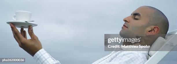 man sitting with head back and eyes closed balancing cup and saucer on tips of fingers - shaved-buzz-cut-back-of-head photos et images de collection