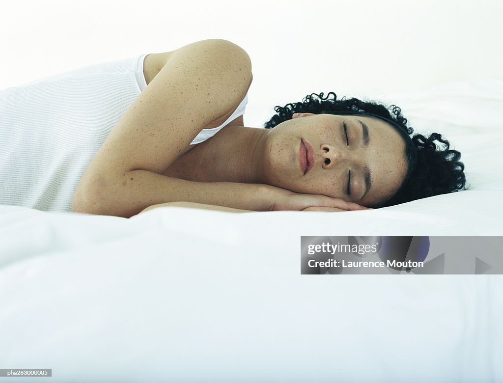 Woman lying on side on bed with hands under head and eyes closed