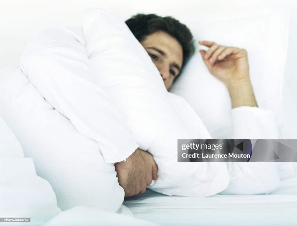 Man lying in bed on side holding pillow