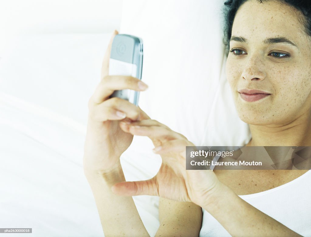 Woman lying on back on bed, looking at cell phone