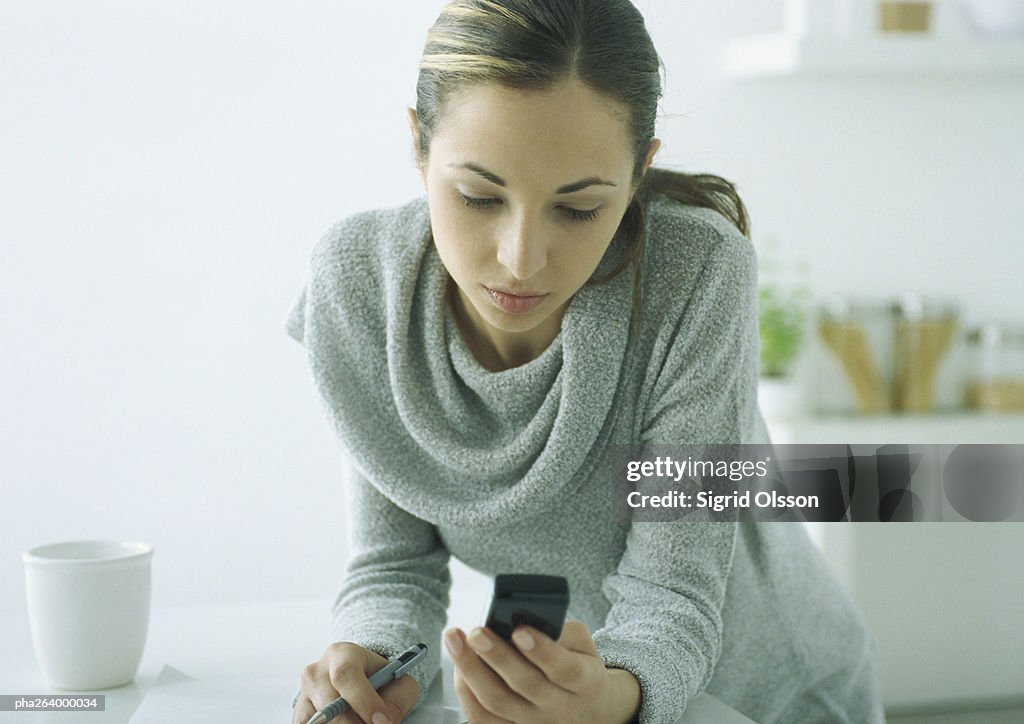 Young woman leaning on table, looking down at cell phone