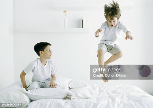 boys on bed, one in mid air - children jumping bed stock pictures, royalty-free photos & images