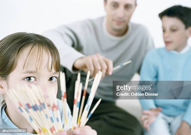 girl holding out pick up sticks, father and boy in background - mikado stock pictures, royalty-free photos & images