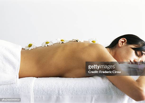 woman lying on stomach, eyes closed, with daisies on bare back, side view - bare back stock-fotos und bilder