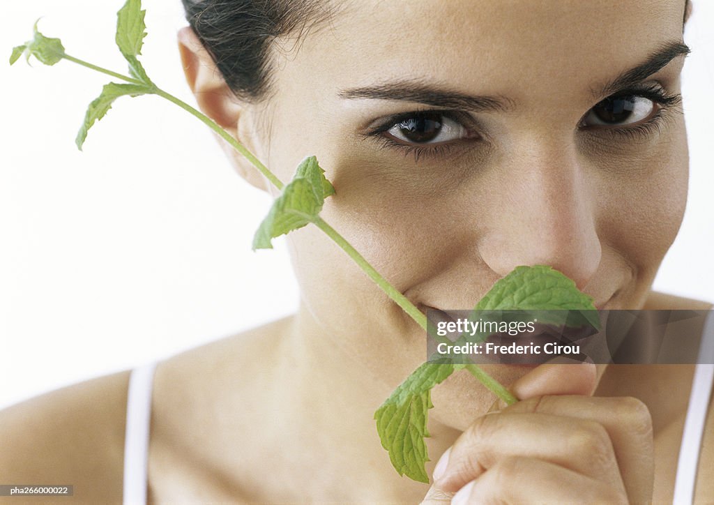 Woman holding sprig of mint to nose, smiling at camera, close-up