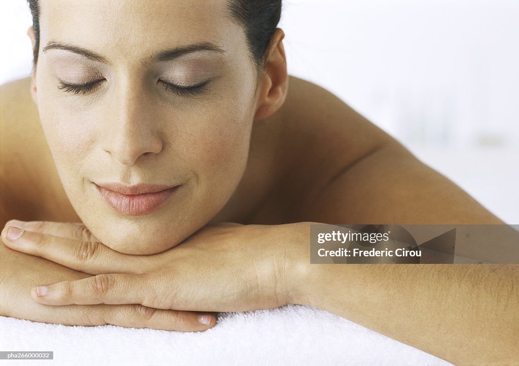 Woman lying with chin resting on hands, eyes closed, close-up