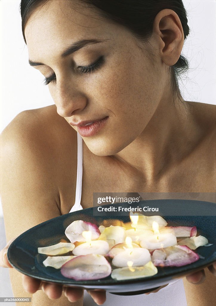 Woman holding plate of candles and rose petals, looking down, close-up