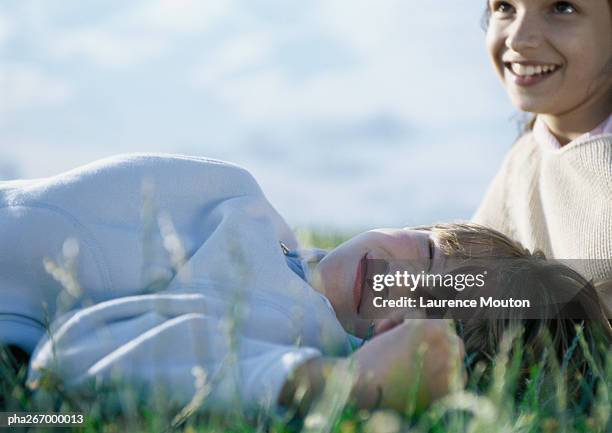 boy lying on grass with eyes closed, girl behind him - happy tween girls lying on grass stock pictures, royalty-free photos & images