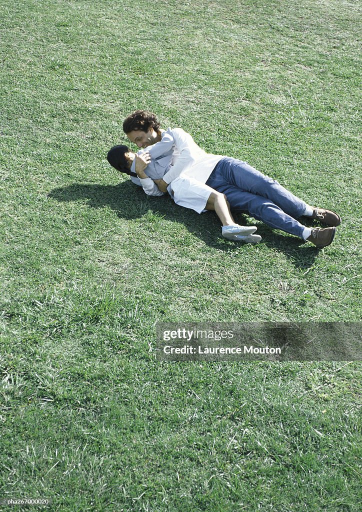 Man and daughter lying on grass in sun, high angle view