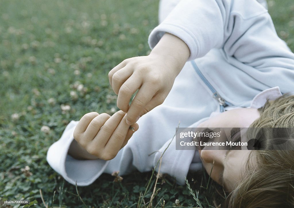 Boy lying on grass holding fingers together in front of face