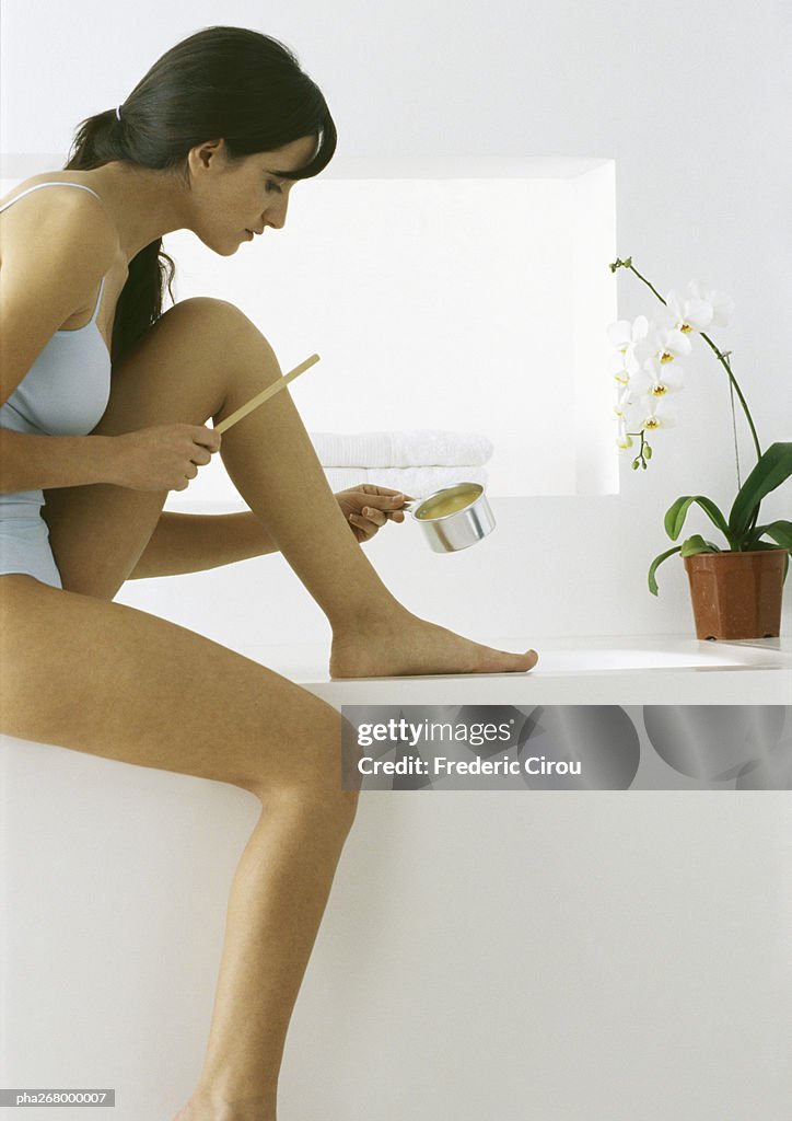 Woman sitting applying hot wax to leg