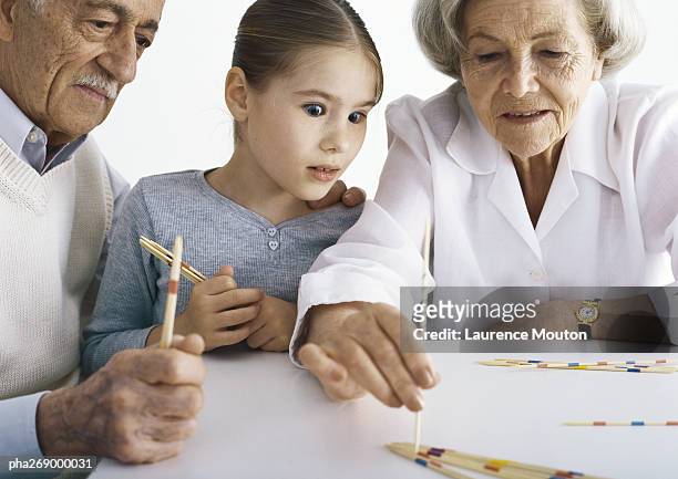 grandparents and girl sitting at table playing pick up sticks - mikado stock pictures, royalty-free photos & images