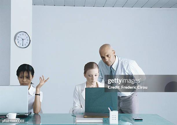 two women sitting at table with laptops, businessman looking over shoulder of one woman - boss over shoulder stock-fotos und bilder