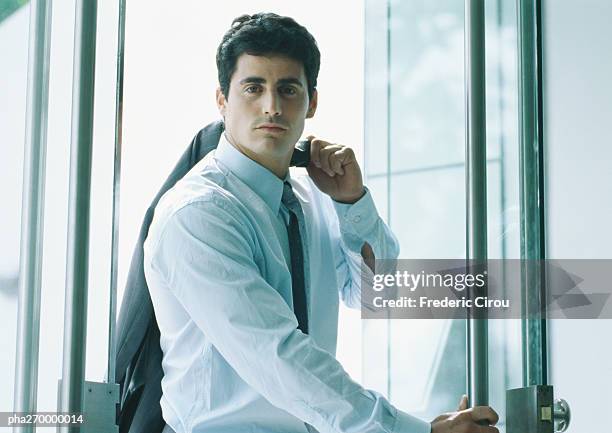businessman holding suit jacket over shoulder, coming through door - door stockfoto's en -beelden