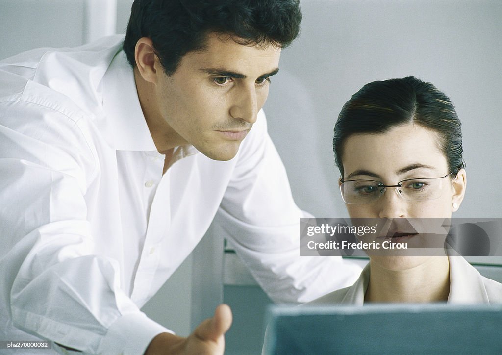 Woman working at computer, man leaning over shoulder gesturing to screen