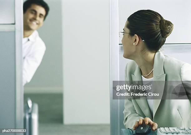 woman sitting at desk looking over shoulder at man looking through door, smiling - door stockfoto's en -beelden