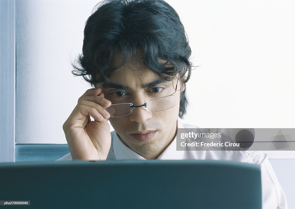 Businessman looking down at computer screen, looking over glasses